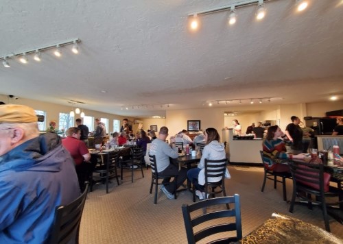 A busy restaurant interior with patrons seated at tables and a bustling kitchen in the background.