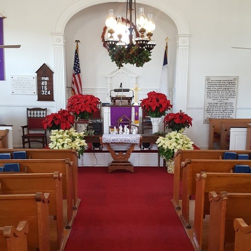 Interior of a church with red and white poinsettias, a pulpit, and festive decorations, viewed from the pews.