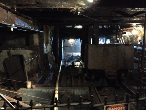 Dimly lit underground mine with rusty tracks and an old cart, surrounded by rough stone walls and safety signs.