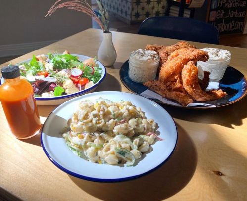 A table with three plates: a salad, fried chicken with sides, and a creamy pasta salad, plus a bottle of hot sauce.