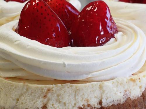 Close-up of a creamy cheesecake topped with whipped cream and glossy strawberries.