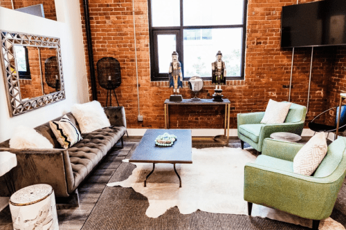 A cozy living room with a brick wall, plush sofa, green chairs, a coffee table, and decorative statues.