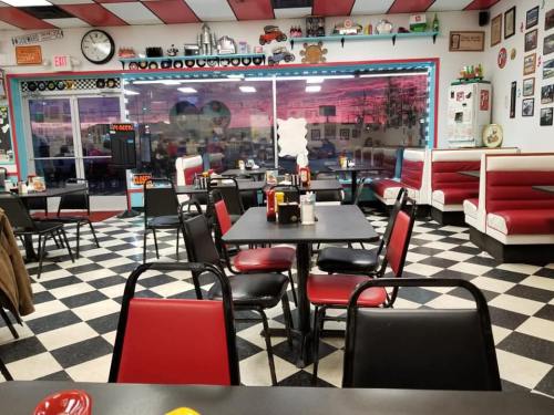 A retro diner interior with checkered floors, red and white booths, and tables set for dining.
