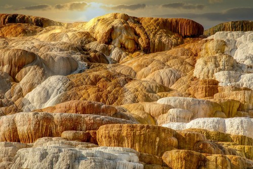 Colorful mineral formations create a textured landscape, with hues of orange, yellow, and white under a soft sunset glow.