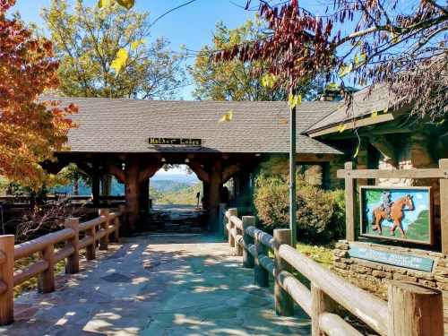 Entrance to a rustic lodge with wooden beams, surrounded by trees and a scenic view in the background.
