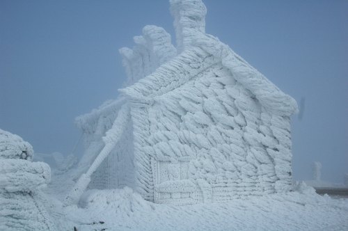 A snow-covered house with thick frost and ice, resembling a winter wonderland scene against a gray sky.