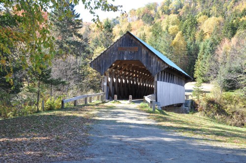 A rustic covered bridge surrounded by colorful autumn trees and a gravel path leading to it.