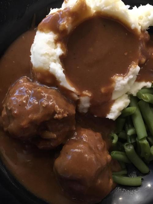 A close-up of a plate featuring meatballs in gravy, mashed potatoes, and green beans.