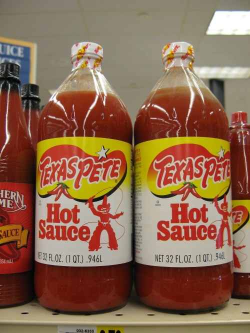 Two large bottles of Texas Pete Hot Sauce on a store shelf, each labeled with a red and yellow design.