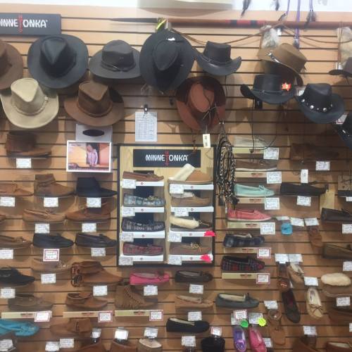 A display of various cowboy hats and moccasins on a wooden wall, with price tags and labels.
