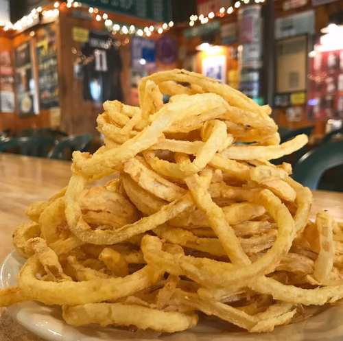 A large pile of crispy, golden onion rings on a plate, set against a cozy restaurant background.