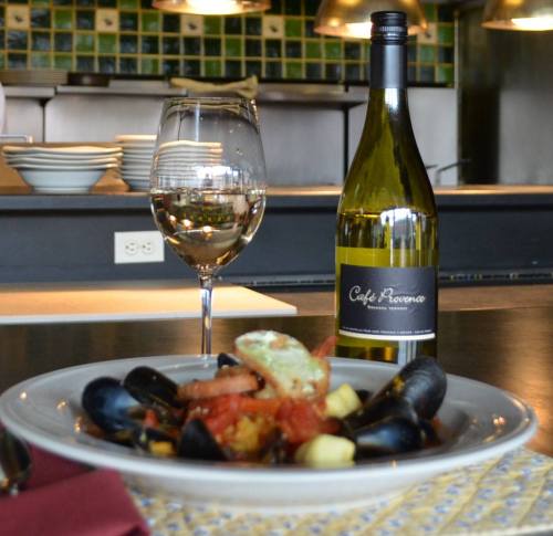 A plate of seafood pasta with mussels, a glass of white wine, and a bottle of Café Romano in a restaurant setting.