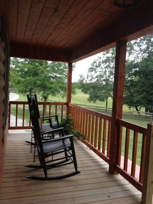 A wooden porch with two rocking chairs overlooking a green landscape and trees.