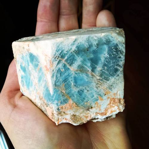 A hand holding a large, rough stone with a blue and white marbled surface and some orange-brown streaks.
