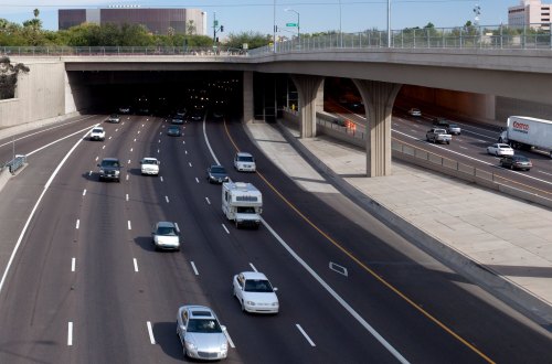 A view of a busy highway with cars entering a tunnel under a bridge on a sunny day.