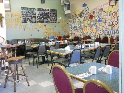 A cozy diner with empty tables, colorful wall murals, and a chalkboard menu in a welcoming atmosphere.