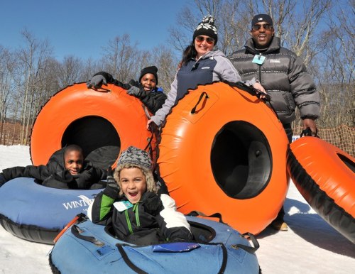 A family enjoys snow tubing, posing with orange and blue tubes in a snowy landscape, smiling and having fun.