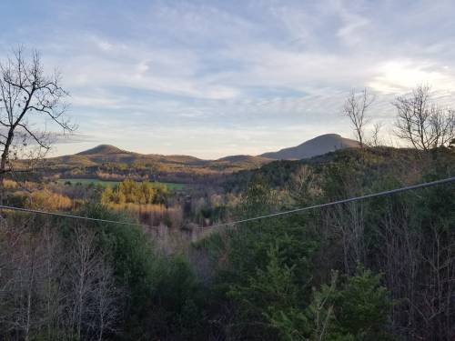 A scenic view of rolling hills and mountains under a clear sky, surrounded by trees and a lush green landscape.