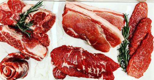 An assortment of raw meats including cuts of beef and pork, garnished with fresh rosemary on a marble surface.