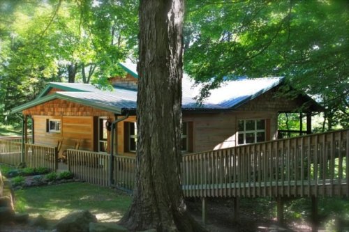 A cozy wooden cabin surrounded by lush green trees and a wooden deck.