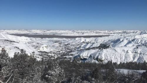 A panoramic view of snow-covered hills and valleys under a clear blue sky.