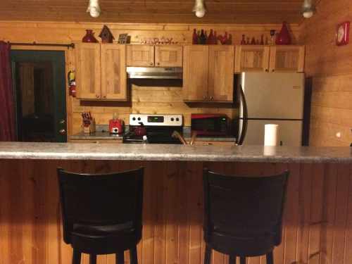 Cozy wooden kitchen with a bar, two stools, stainless steel appliances, and rustic decor.