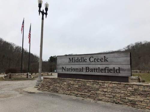 Sign for Middle Creek National Battlefield, with flags and a stone base, set against a cloudy sky.