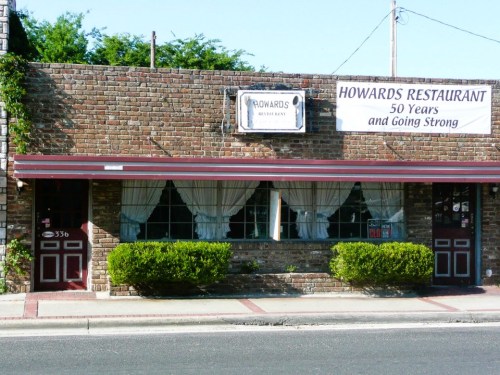 A brick building with a sign reading "Howard's Restaurant: 50 Years and Going Strong," featuring white curtains in the windows.