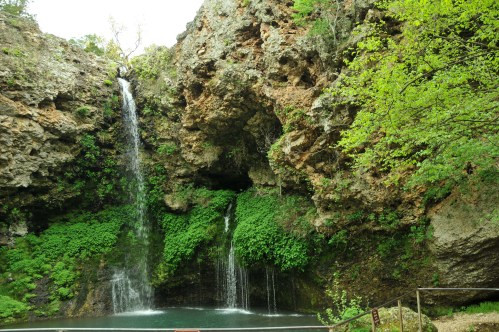 A serene waterfall cascading over rocky cliffs, surrounded by lush green foliage and a tranquil pool below.