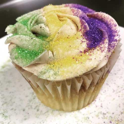 A colorful cupcake topped with swirls of frosting in green, purple, and yellow, sprinkled with glitter.