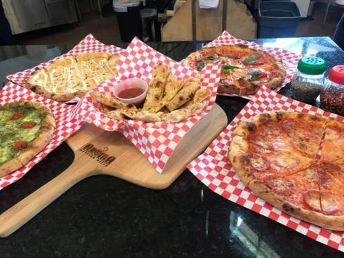 A variety of pizzas on a table, including a margherita, pesto, and a side of breadsticks, all in red-checkered baskets.