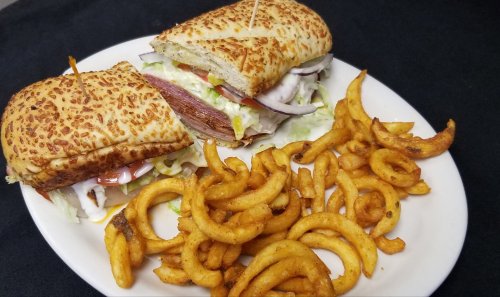 A toasted sandwich filled with lettuce, tomatoes, and meat, served with a side of curly fries on a white plate.