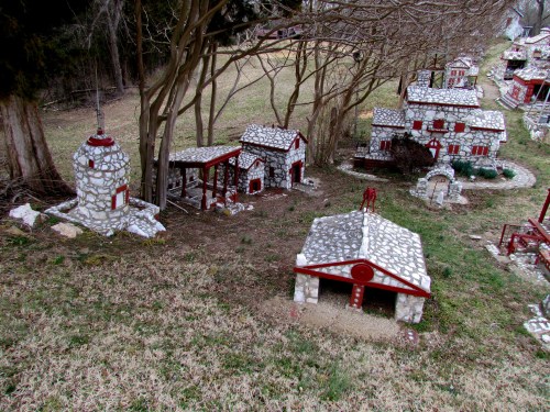 A miniature village with stone buildings and red accents, set in a grassy area under trees.