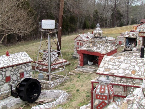 A miniature village with stone buildings, a water tower, and a grassy area, set in a rural landscape.