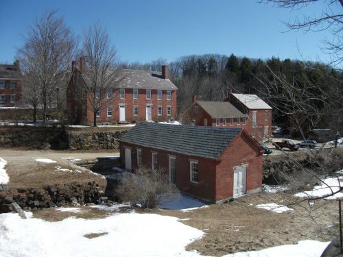 Historic brick buildings surrounded by snow and bare trees under a clear blue sky.