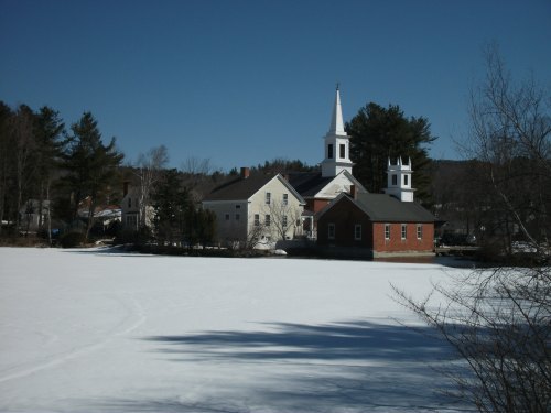 A snowy landscape featuring a small town with a church and buildings against a clear blue sky.