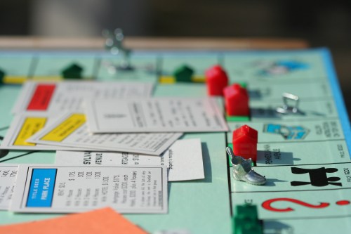 Close-up of a Monopoly game board with property cards, houses, and game pieces scattered across the surface.