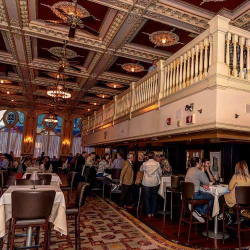 Elegant restaurant interior with ornate ceilings, chandeliers, and a bustling atmosphere of diners and staff.
