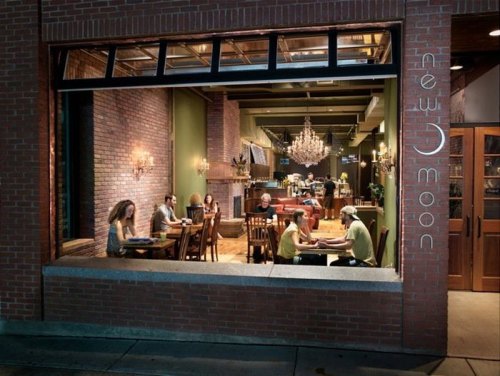 A cozy restaurant interior with diners at tables, exposed brick walls, and elegant chandeliers.