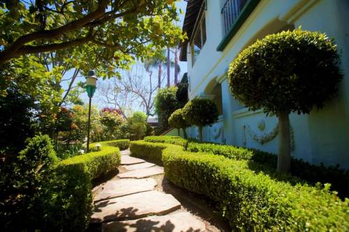A stone pathway winds through neatly trimmed hedges and round topiary trees, leading to a charming white building.
