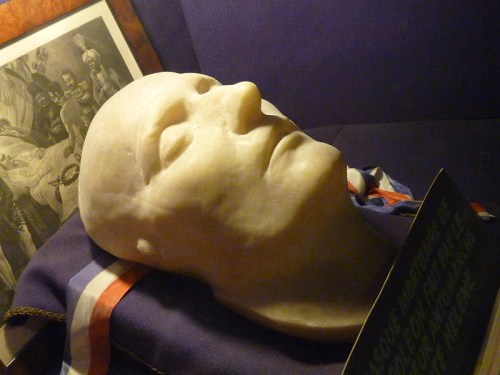 A lifelike sculpted head displayed on a draped cloth, surrounded by historical images and artifacts.