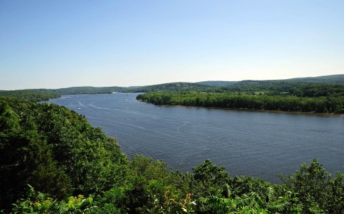 A serene river flows through lush green hills under a clear blue sky.