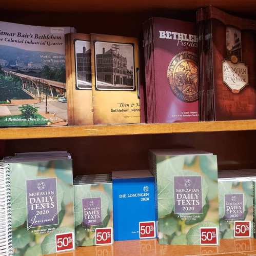 Books displayed on a shelf, including "Bethlehem Profiles" and "Moravian Daily Texts 2020," with sale tags.