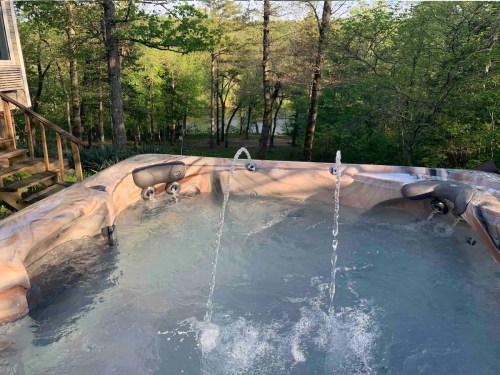 A hot tub with water jets, surrounded by trees and overlooking a serene landscape.