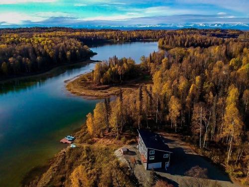 Aerial view of a serene lake surrounded by autumn-colored trees and a house near the water's edge.