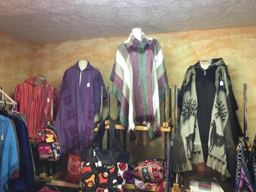 Display of colorful ponchos and bags in a cozy shop, showcasing various patterns and textures.