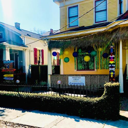 Colorful decorations adorn a yellow house with a thatched roof, celebrating a festive occasion in a vibrant neighborhood.