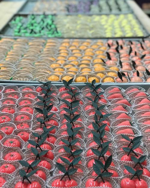 A colorful display of assorted candies arranged in rows, featuring red, orange, and green treats with decorative leaves.