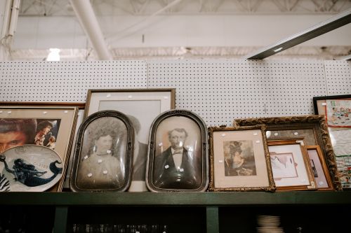 A display of vintage framed portraits and artwork on a shelf, with various styles and sizes of frames.
