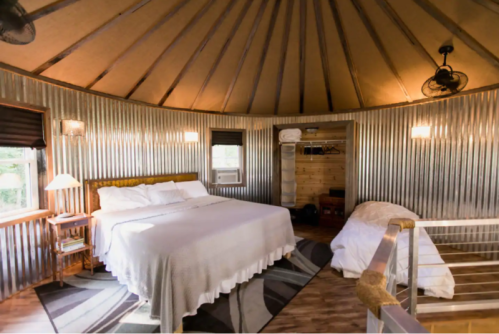 Cozy circular bedroom with a large bed, wooden accents, and modern amenities in a rustic setting.